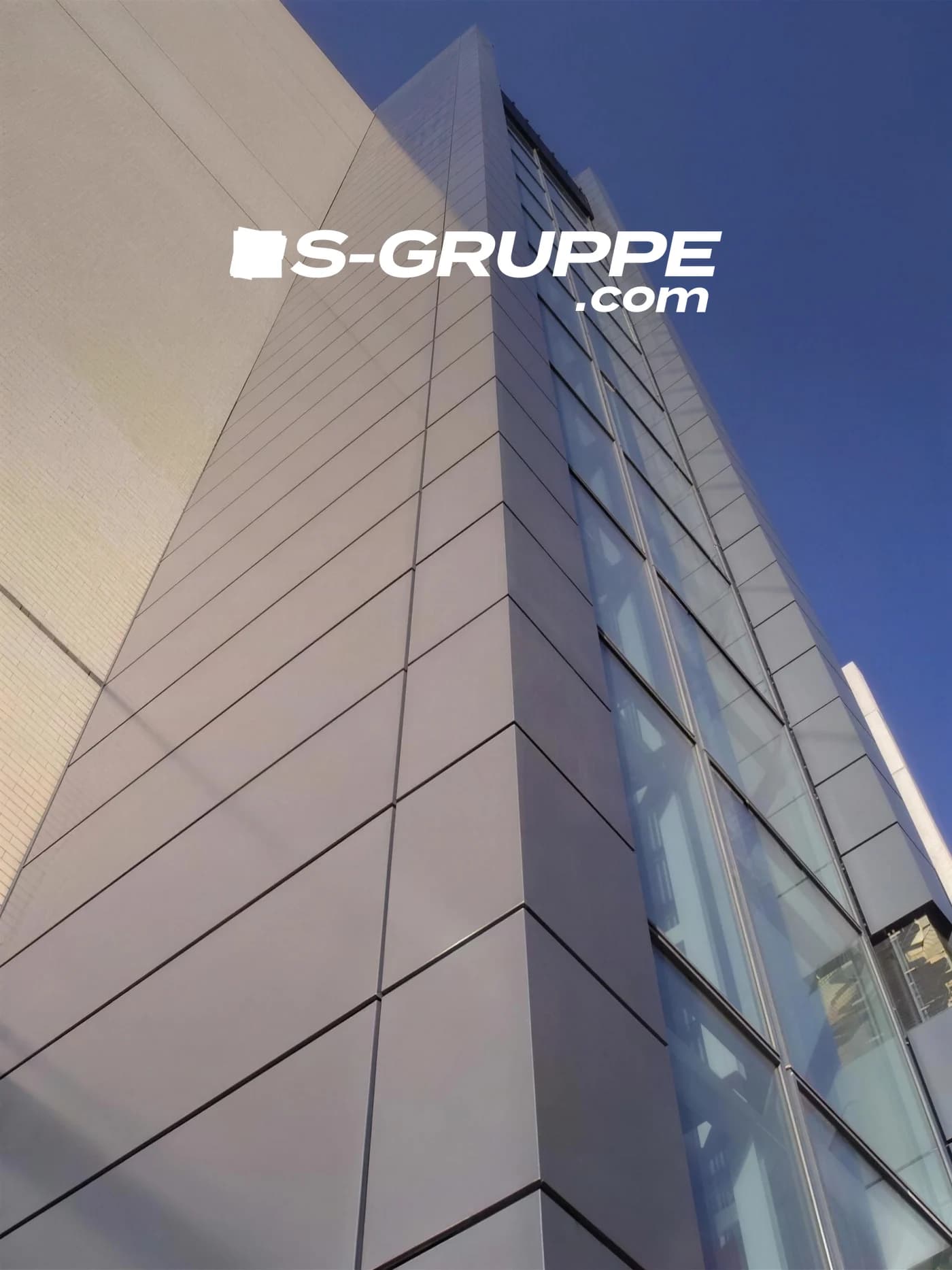 Kunde S-Gruppe: eine Fassade aus grossformatigen Metallpaneelen von unten gegen den blauen Himmel, darüber die Wortmarke des Kunden.
